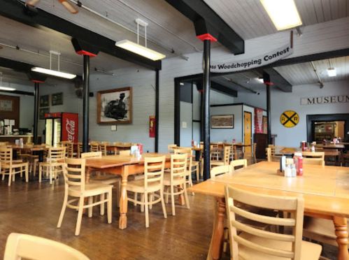 Interior of a rustic restaurant with wooden tables and chairs, featuring a museum display and vintage decor.