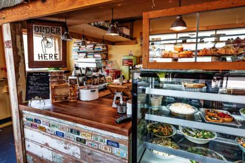 A cozy café counter with a menu board, books, and a display of fresh salads and pastries.