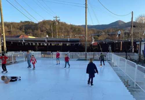 Children ice skating on an outdoor rink with mountains in the background and a clear blue sky.