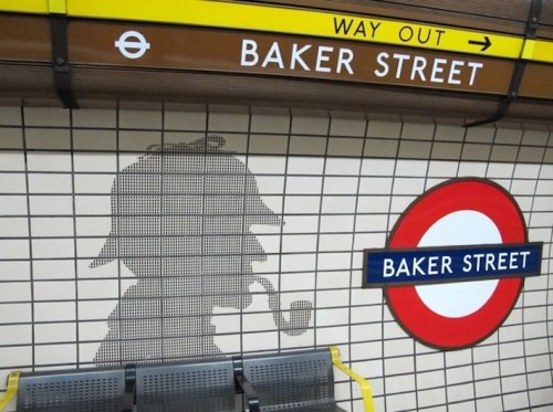 A wall at Baker Street station features a silhouette of Sherlock Holmes with a pipe, alongside the station sign.