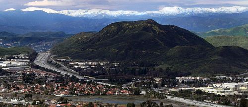 A panoramic view of a mountainous landscape with snow-capped peaks in the background and a highway running through a valley.