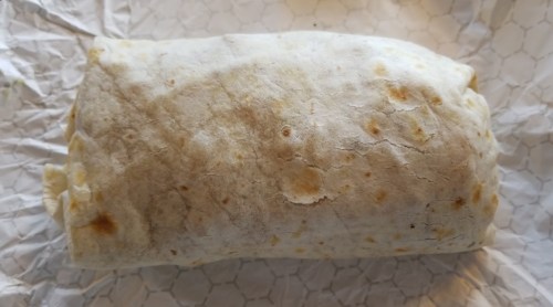 A wrapped burrito on crumpled paper, showcasing a lightly toasted tortilla.