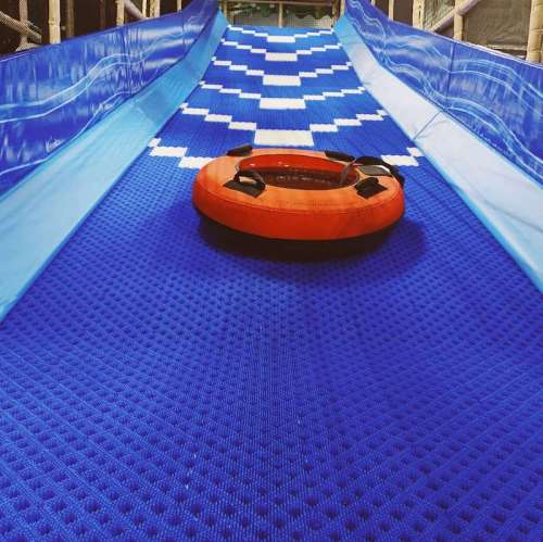 A colorful water slide with a blue surface and an orange inner tube at the bottom, ready for sliding.