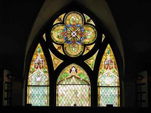 Colorful stained glass window featuring intricate floral and geometric designs in a gothic style.
