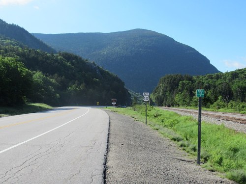 A scenic view of a highway alongside a mountain, with road signs indicating exit and mile markers.