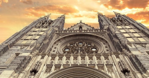Gothic cathedral facade with intricate details, towering spires, and a dramatic sunset sky in the background.