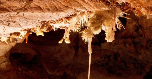 Stalactites and mineral formations hanging from a cave ceiling, illuminated by soft light.
