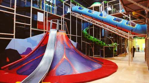 Colorful indoor playground featuring a volcano slide, climbing structures, and a large blue slide.