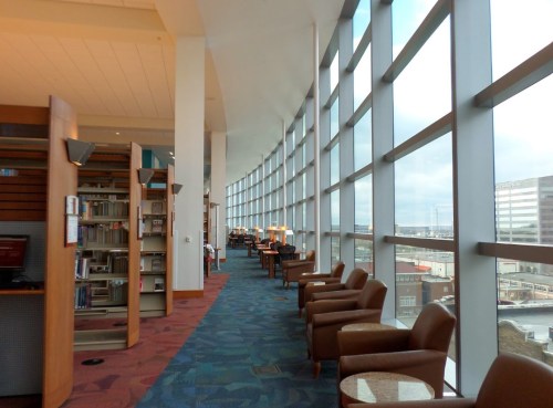 A modern library interior with large windows, bookshelves, and comfortable seating along a curved wall.