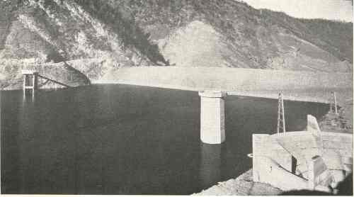 A black and white image of a dam with a reservoir, surrounded by rocky hills and a concrete structure in the foreground.