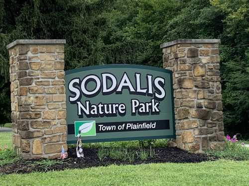 Sign for Sodalis Nature Park in Plainfield, featuring stone pillars and greenery in the background.