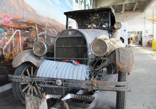 A vintage, weathered car with a rusty exterior, displayed in a spacious, industrial setting.