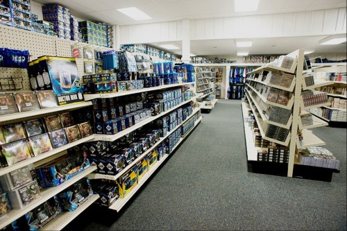 A well-organized store aisle filled with shelves of DVDs, games, and merchandise, with bright lighting and a clean layout.