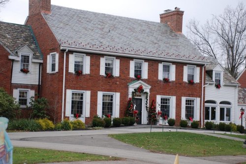 A large brick house decorated with holiday wreaths and red bows, surrounded by greenery and a well-maintained lawn.