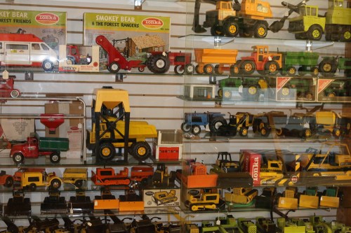 A display of vintage toy trucks and construction vehicles in various colors and styles on a wall-mounted shelf.