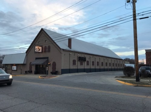 A large, brick building with a sloped roof, featuring a sign and surrounded by power lines and a street.
