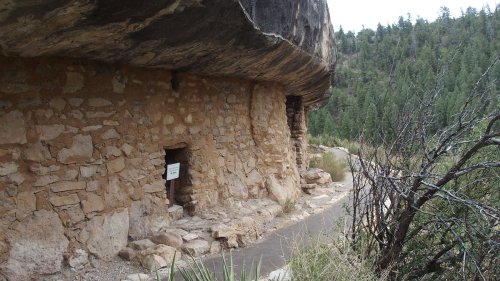 Ancient stone structure built into a cliffside, surrounded by greenery and a pathway leading to the entrance.