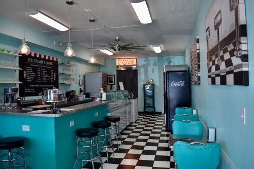A bright ice cream shop with teal walls, black and white checkered floor, and retro-style seating.