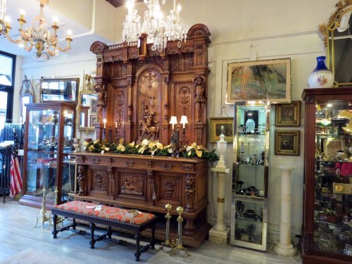 Intricately carved wooden display with ornate details, surrounded by vintage decor and glass showcases in a charming shop.