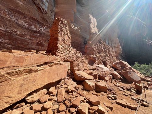 Ancient stone ruins amidst red rock formations, with sunlight streaming down in a canyon setting.