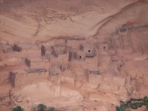 Ancient cliff dwellings built into a rocky landscape, showcasing stone structures and wooden supports.