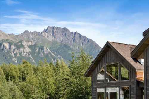 A mountain view with lush greenery and a modern wooden house in the foreground under a clear blue sky.