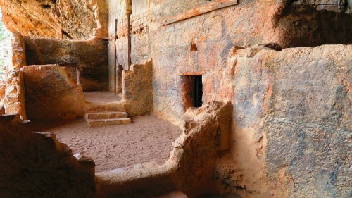 Ancient cave interior with textured walls, steps, and a small opening, showcasing natural rock formations.