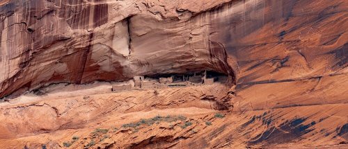 Ancient cliff dwellings nestled in a sandstone rock face, showcasing rich red and orange hues of the landscape.