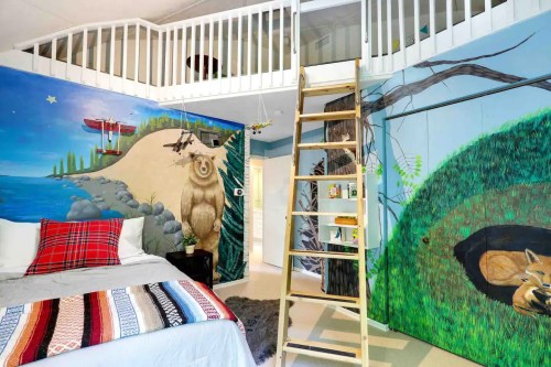 A cozy bedroom with a loft, featuring colorful murals of nature, a ladder, and a bed with a patterned blanket.