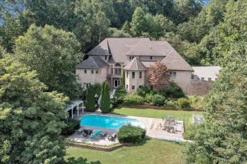 Aerial view of a large house surrounded by trees, featuring a pool and outdoor seating area in the backyard.
