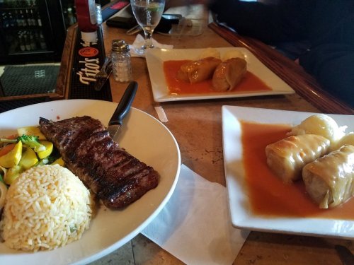 A plate with grilled steak, rice, and vegetables, alongside another plate of stuffed cabbage rolls in sauce.