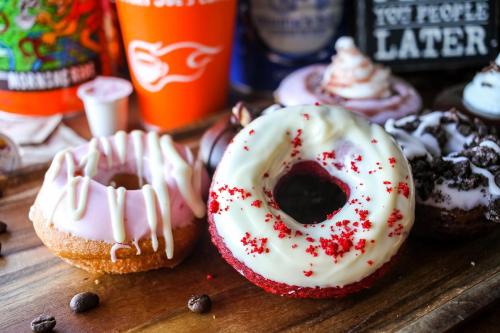 A variety of colorful donuts on a wooden surface, including a red velvet donut and one with pink icing.