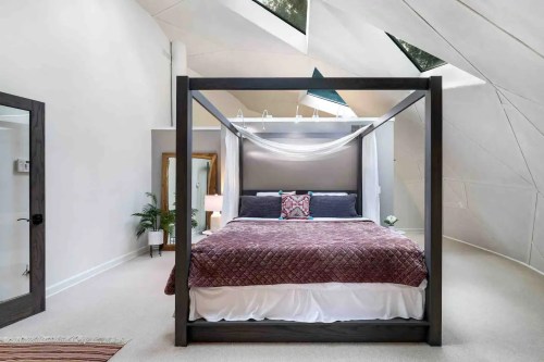 A modern bedroom featuring a four-poster bed with a quilt, skylights, and unique architectural walls.