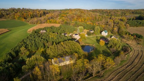 Aerial view of a rural landscape with a pond, surrounded by trees and colorful autumn foliage.