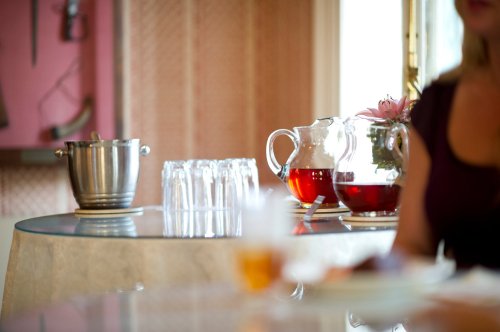 A table setting with a pitcher of tea, a glass pitcher with flowers, and a silver ice bucket in a softly lit room.