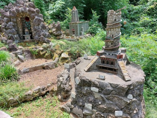 Miniature stone structures surrounded by greenery, featuring intricate designs and varying heights.