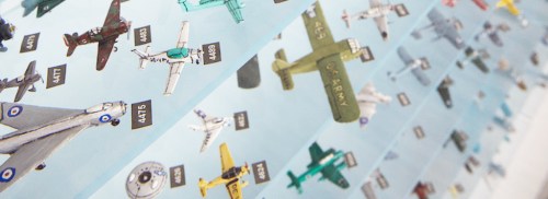 A display of various model airplanes arranged in rows, showcasing different colors and designs against a light background.