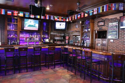 A cozy bar with a wooden counter, colorful lights, and international flags hanging above. TVs display sports events.