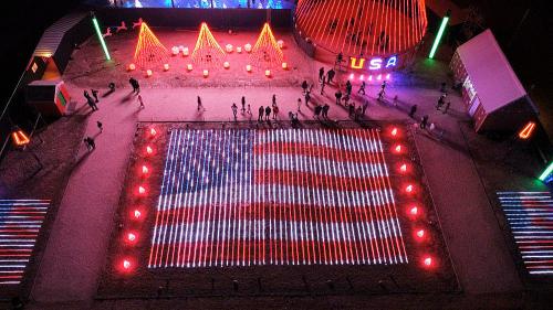 Aerial view of a large illuminated American flag display with colorful lights and people walking around.