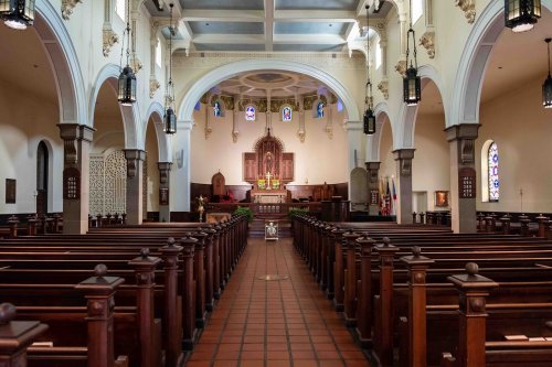 Interior of a church featuring wooden pews, arched ceilings, stained glass windows, and a central altar.