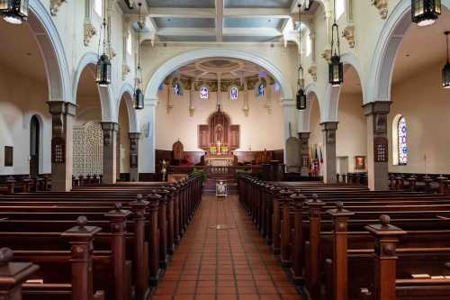 Interior of a church featuring wooden pews, arched ceilings, stained glass windows, and a central altar.