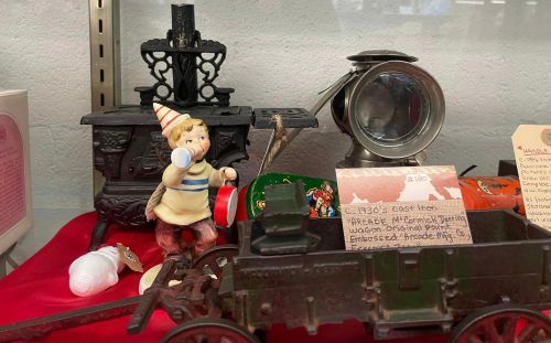 A vintage display featuring a toy train, a figurine with a drum, and various nostalgic items on a red cloth.