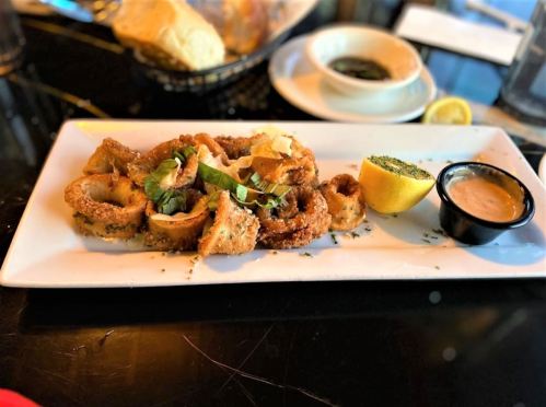 A plate of crispy fried calamari garnished with herbs, served with a lemon wedge and dipping sauce.
