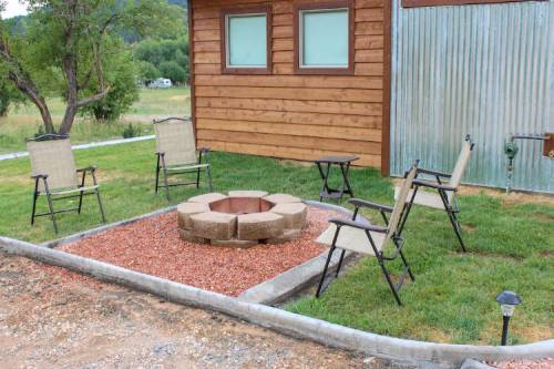 A cozy outdoor fire pit area with stone seating and chairs, surrounded by grass and a wooden building.
