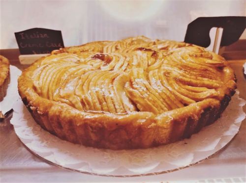 A golden-brown Italian cream cake with a decorative swirl pattern on top, displayed on a white lace doily.