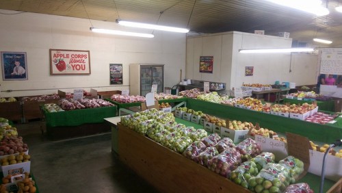 A bright market filled with various apples and other fruits in bags, with signs and posters on the walls.