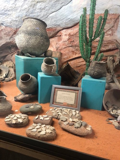 Display of ancient pottery and artifacts, including woven baskets and stone tools, set against a desert backdrop.