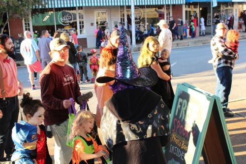 A crowd in costumes gathers for a Halloween event, with a sign for free photos and festive decorations in the background.