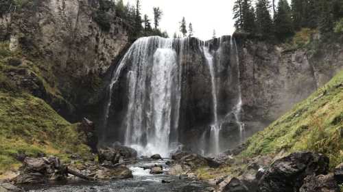 A majestic waterfall cascading down rocky cliffs, surrounded by lush greenery and mist rising from the water.