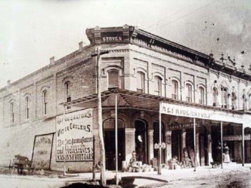 Historic building with a sign for stoves, featuring a covered porch and vintage advertisements on the exterior.